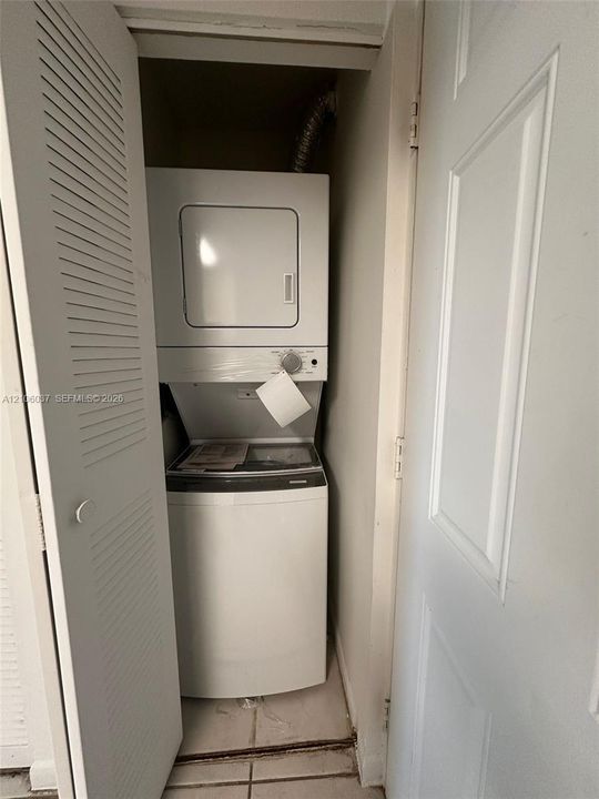 Laundry closet featuring a white stacked washer and dryer unit, louvered closet doors, and tile flooring