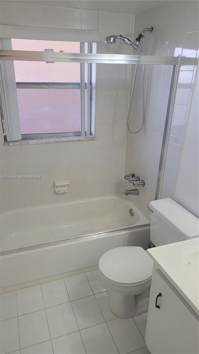 FULL BTH featuring a tub-shower combination with a handheld showerhead, sliding glass enclosure, white tile walls, a porcelain toilet, and a white vanity
