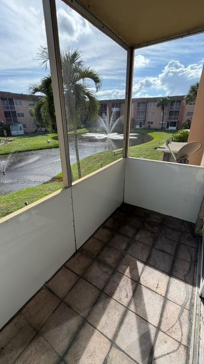 Screened-in BALCONY featuring tile flooring and metal frame construction, overlooking a pond with a water feature and manicured lawn