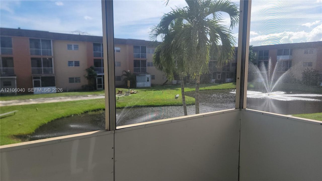 Screened-in balcony featuring an exterior solid wall panel, palm trees, and a water feature with a fountain
