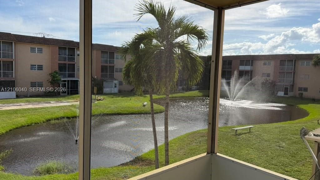 Screened BALCONY VIEW featuring metal framing, overlooking a pond with decorative water fountains, manicured lawn, and mature palm trees