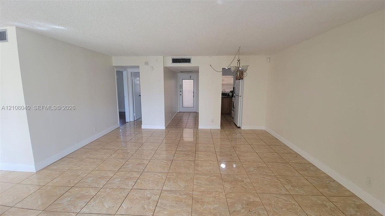 Open-concept interior featuring large-format ceramic tile flooring, neutral wall finishes, a multi-light chandelier fixture, and a glass-paneled exterior door