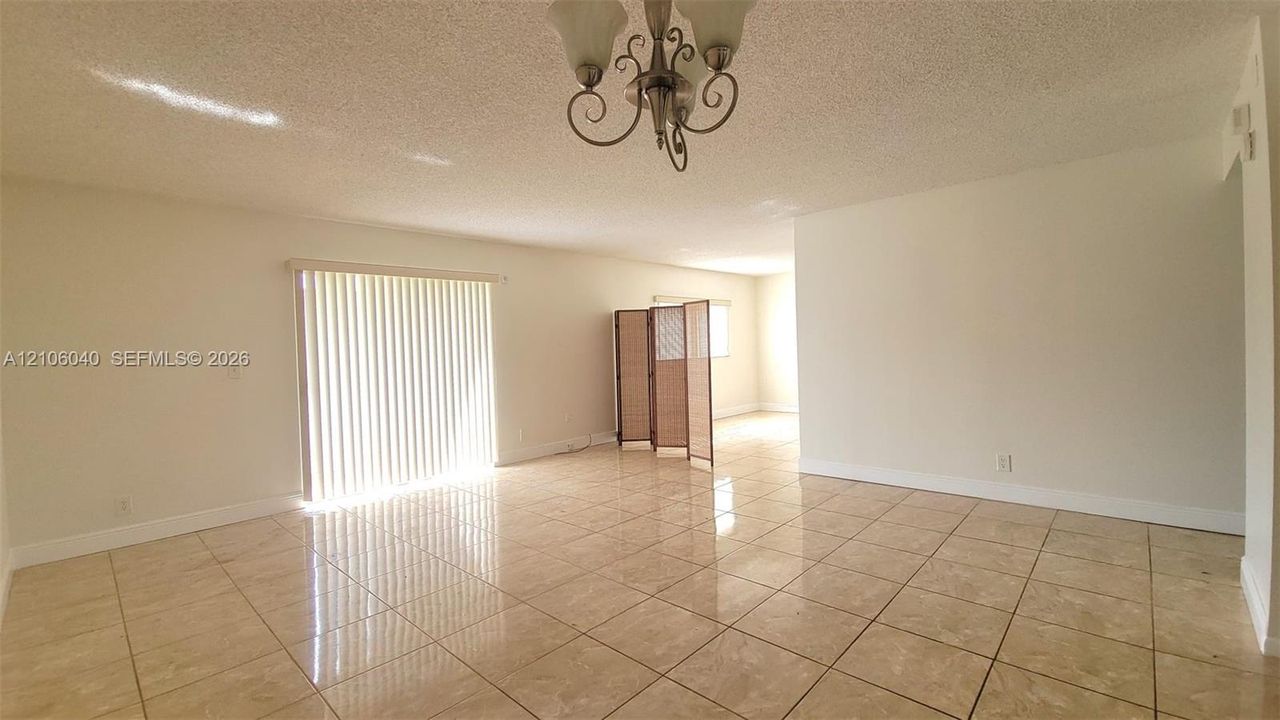 Open Living Space tile flooring, textured ceiling, multi-arm chandelier, and sliding glass door with vertical blinds