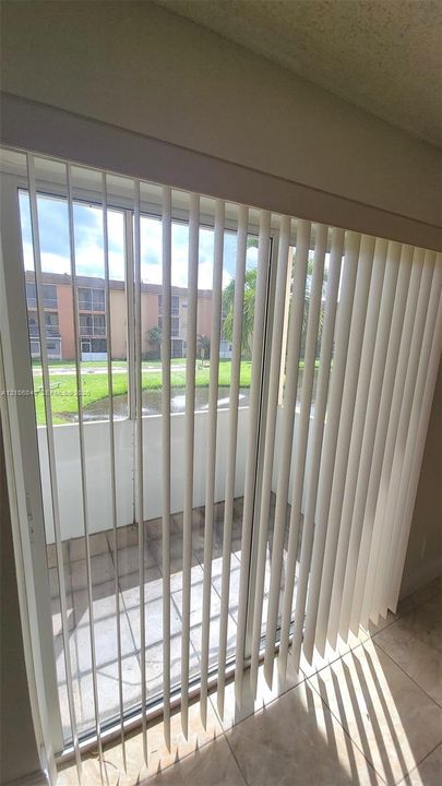 BALCONY Sliding glass door with vertical blinds opening to a screened-in balcony featuring tile flooring