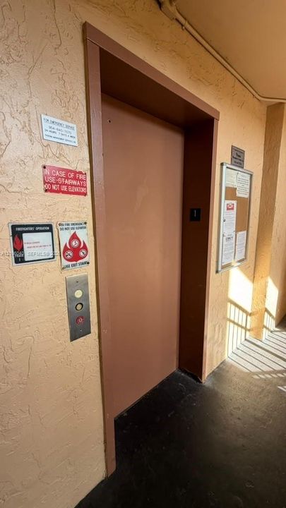 ELEVATOR access featuring a metal door, brushed metal push-button interface, and textured wall finish