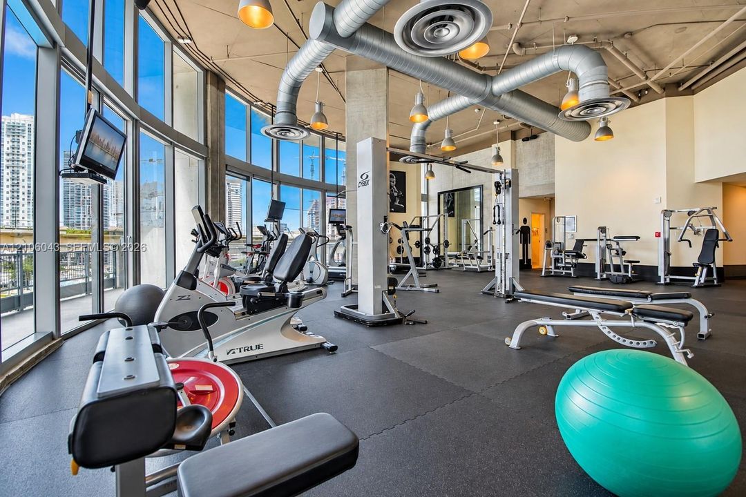 Fitness center featuring floor-to-ceiling windows, exposed concrete ceilings, industrial-style ductwork, and rubberized flooring