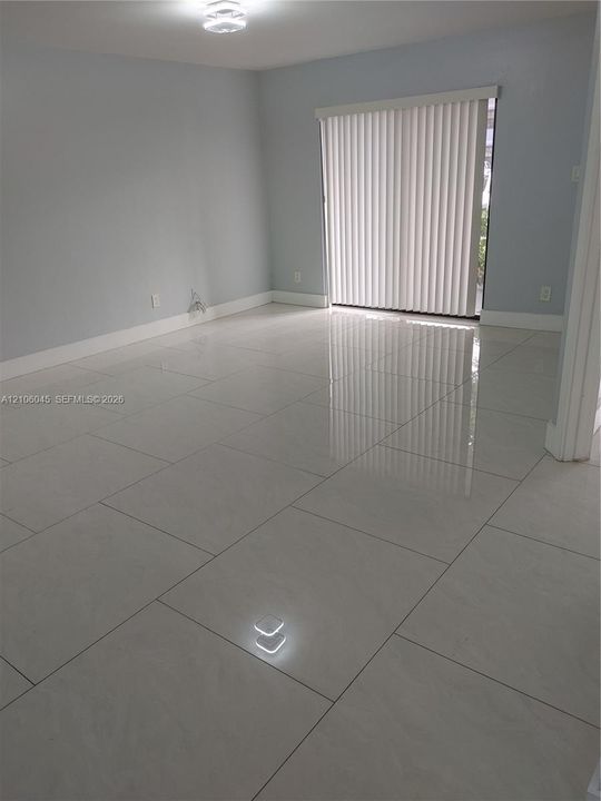 Neutral-toned interior featuring large-format polished tile flooring, light-reflective surfaces, a sliding glass door, and a flush-mount ceiling light fixture