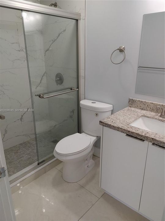 Walk-in shower with floor-to-ceiling large-format tile surround, frameless glass door, vanity with speckled stone-finish countertop, and polished chrome fixtures