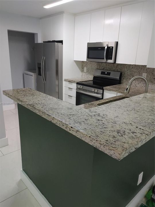 Kitchen featuring stone countertops, white shaker-style cabinetry, stainless steel appliances, and a breakfast bar