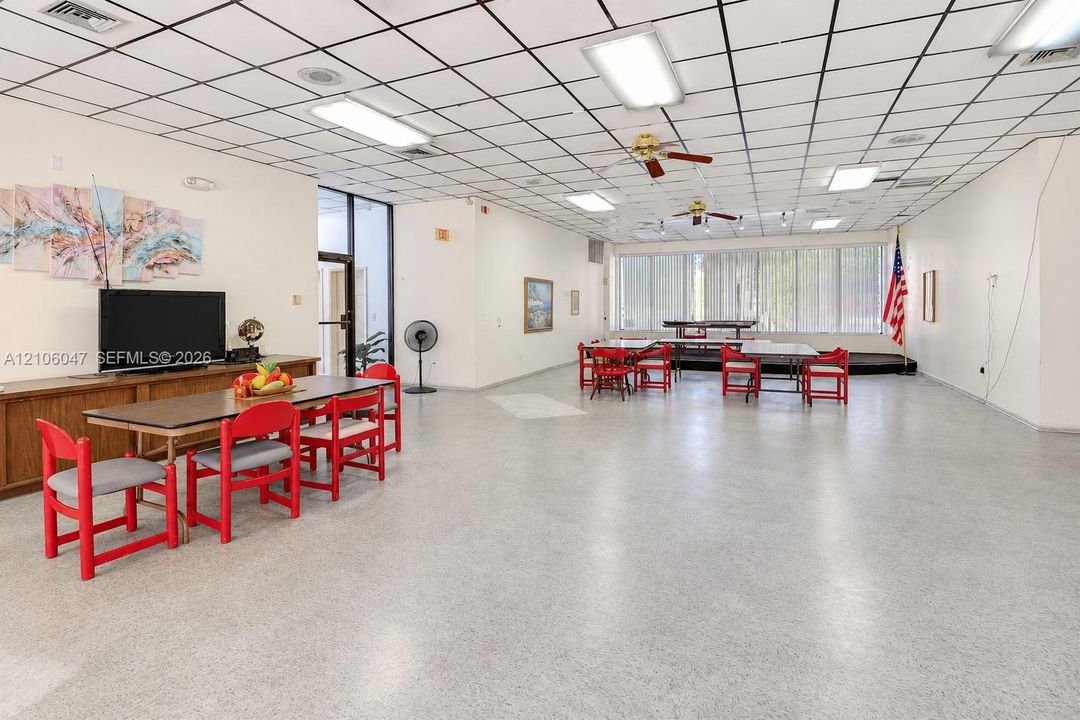 Open-concept interior space featuring a suspended drop ceiling, recessed and flush-mount fluorescent lighting, dual ceiling fans, floor-to-ceiling windows, and resilient composition flooring