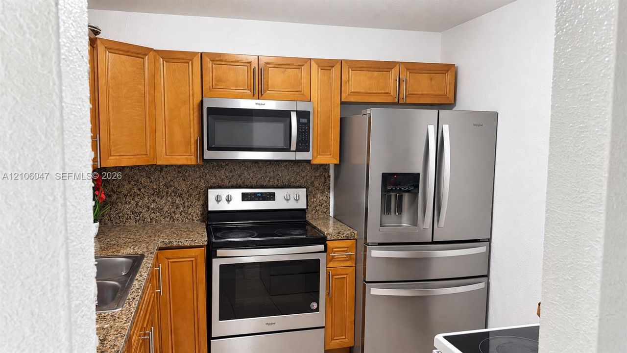 Kitchen featuring wood cabinetry, stone-finish countertops, and a suite of stainless steel appliances including a double-door refrigerator, microwave, and range
