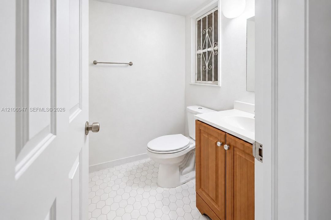 Bathroom featuring hexagon tile flooring, wood-finish vanity with a white countertop, wall-mounted hardware, and a window with decorative security bars