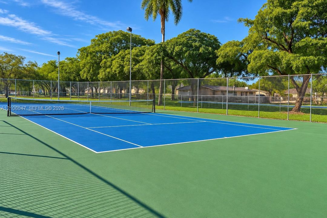 Tennis court with high-contrast blue and green acrylic surfacing, perimeter chain-link fencing, and overhead court lighting