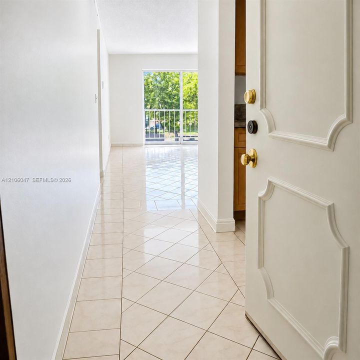Entryway featuring tile flooring laid in a diamond pattern, white interior walls, a paneled door with polished brass hardware, and a sliding glass door with a metal balcony railing