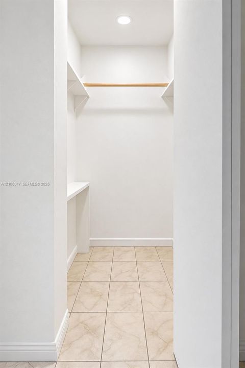 Walk-in closet featuring stone-finish tile flooring, recessed ceiling lighting, built-in shelving, and a wood-finish hanging rod