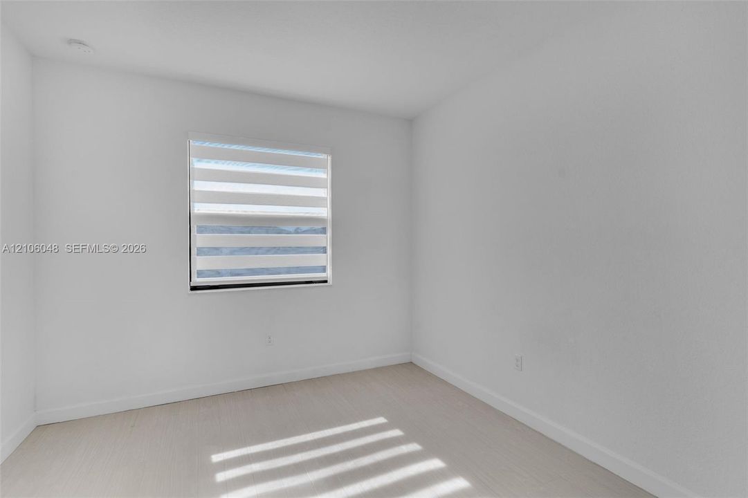 Neutral interior featuring crisp white walls, light-toned wood-finish flooring, and a window equipped with horizontal zebra-style blinds
