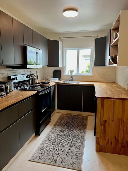 Kitchen featuring dark flat-panel cabinetry, wood-finish countertops, white subway tile backsplash, and stainless steel undermount sink