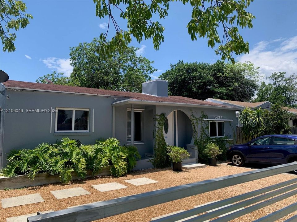 Single-story exterior featuring a arched entryway, grey smooth-finish siding, gravel landscaping, and concrete paver walkway