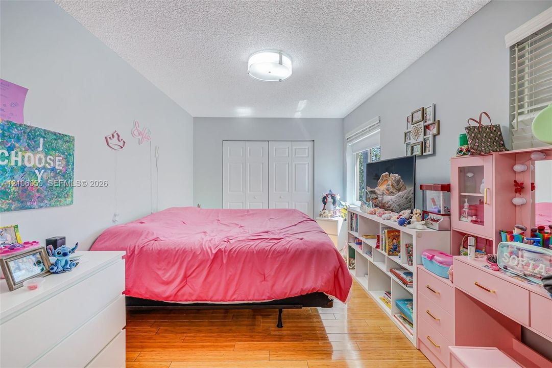 Wood-finish flooring, white double-door reach-in closet, flush-mount ceiling light fixture, and windows with horizontal blinds