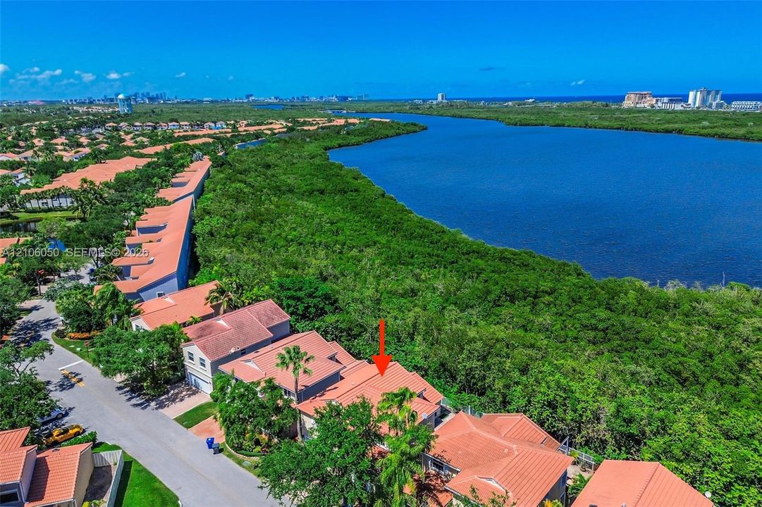 Aerial perspective featuring terracotta-style roofing, two-story structural design, and proximity to coastal water and native vegetation