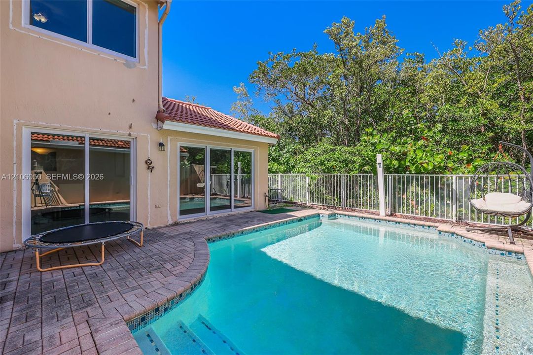Backyard featuring an in-ground pool with built-in stairs, paver stone decking, and white metal fencing