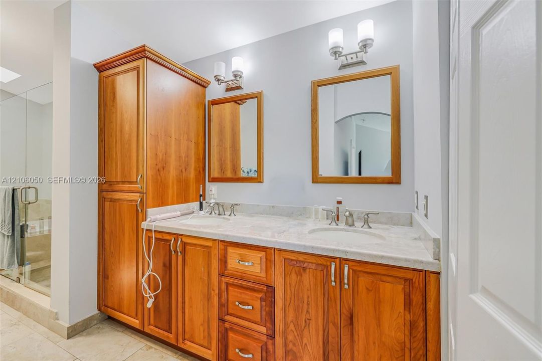 Double vanity featuring a light-toned stone countertop, wood cabinetry with integrated floor-to-ceiling storage, two wall-mounted mirrors with wood frames, and dual brushed-nickel wall sconces