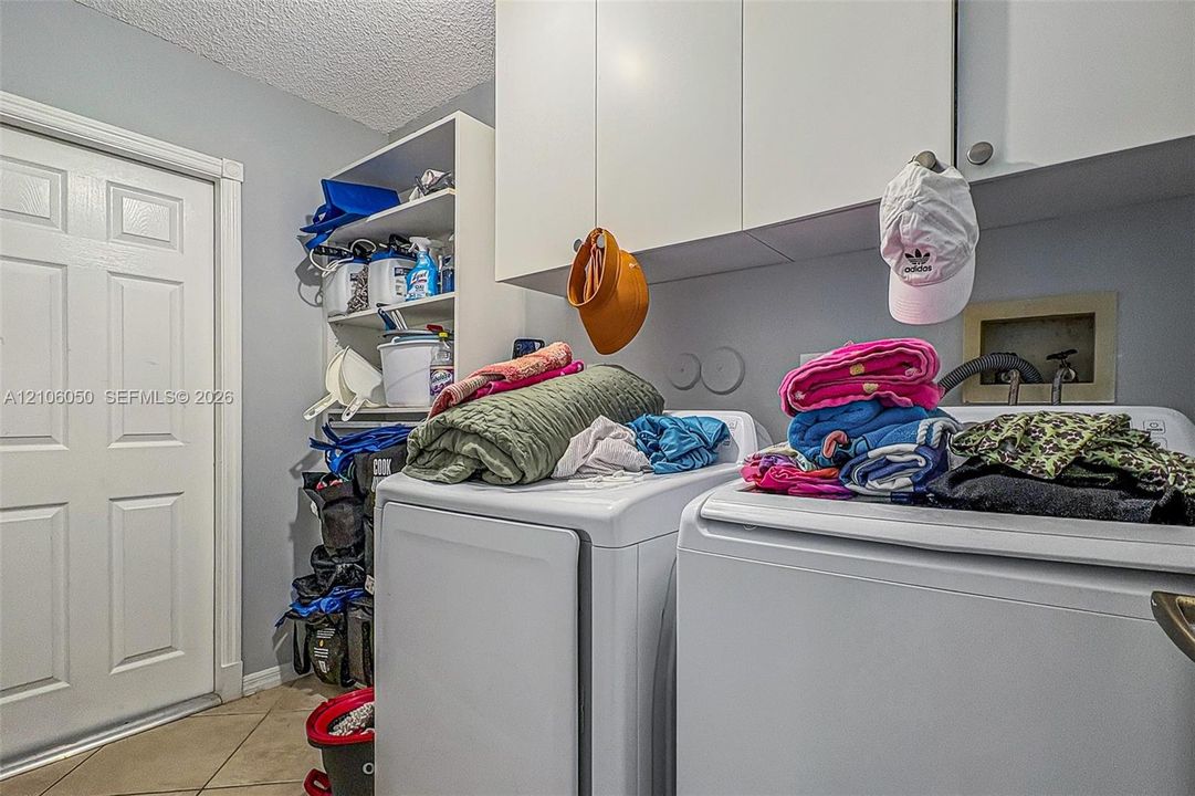 Laundry room featuring white wall-mounted cabinetry, open shelving, and tile flooring