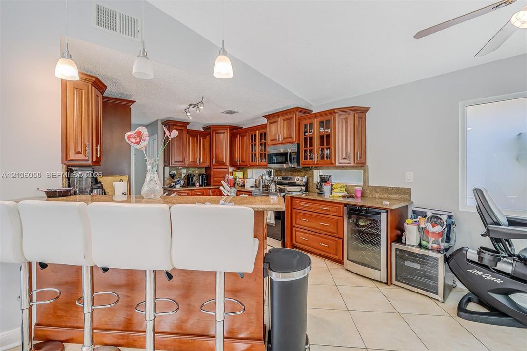 Kitchen featuring wood cabinetry, stone countertops, breakfast bar, and under-counter beverage refrigerator