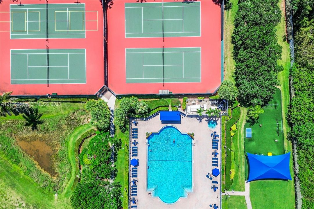 Recreational complex featuring four tennis courts, a swimming pool, a separate spa, and a shaded outdoor area with turf