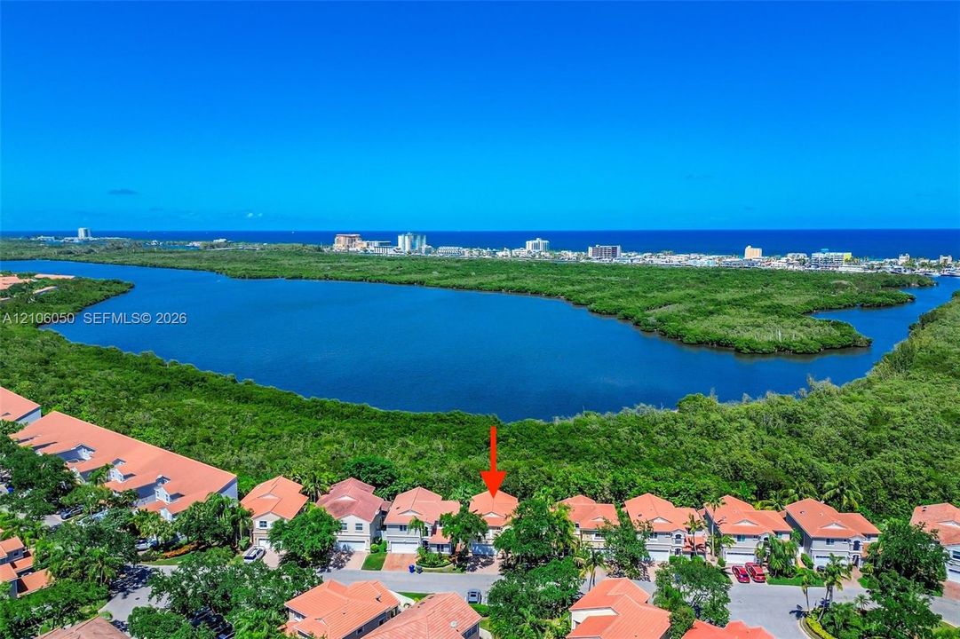 Aerial perspective of a multi-story residence with a tiled roof, situated within a coastal community featuring proximity to a large water basin and dense greenery