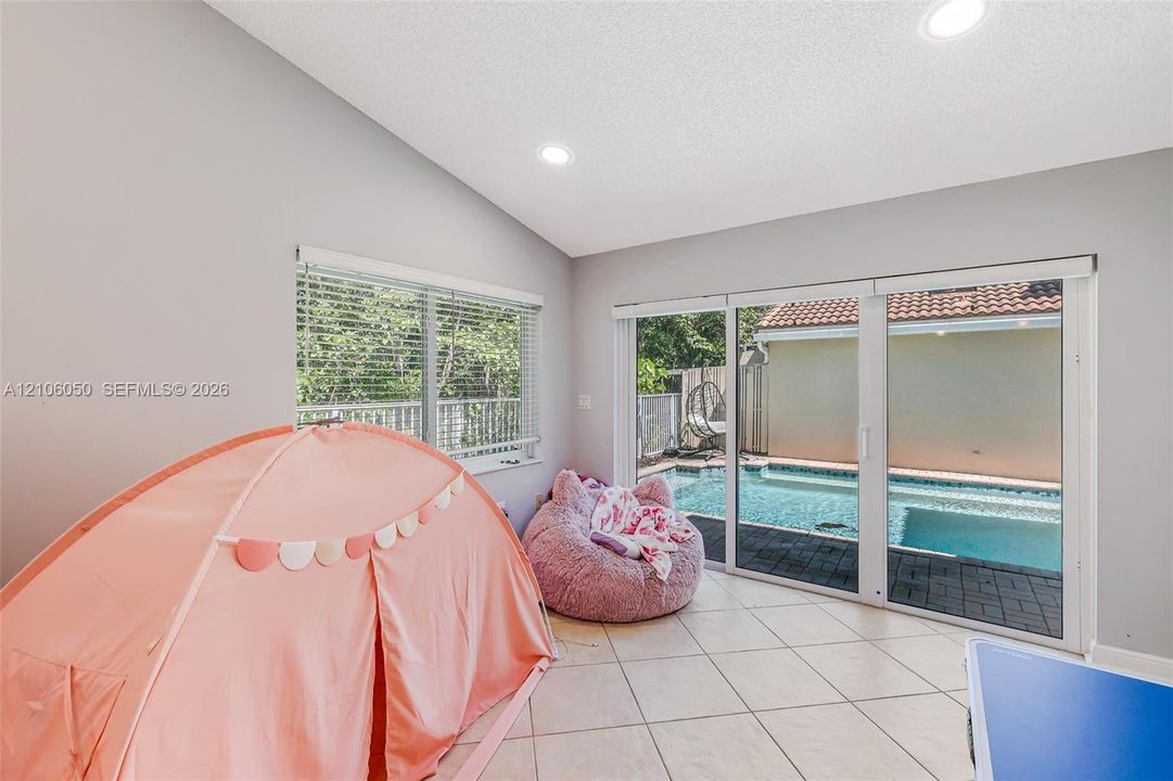 Vaulted ceiling featuring recessed lighting, large-format tile flooring, and sliding glass doors opening to an exterior swimming pool