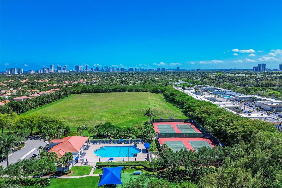Expansive outdoor recreational complex featuring two fenced tennis courts, a swimming pool with paved deck, and a clubhouse with a clay-tile roof
