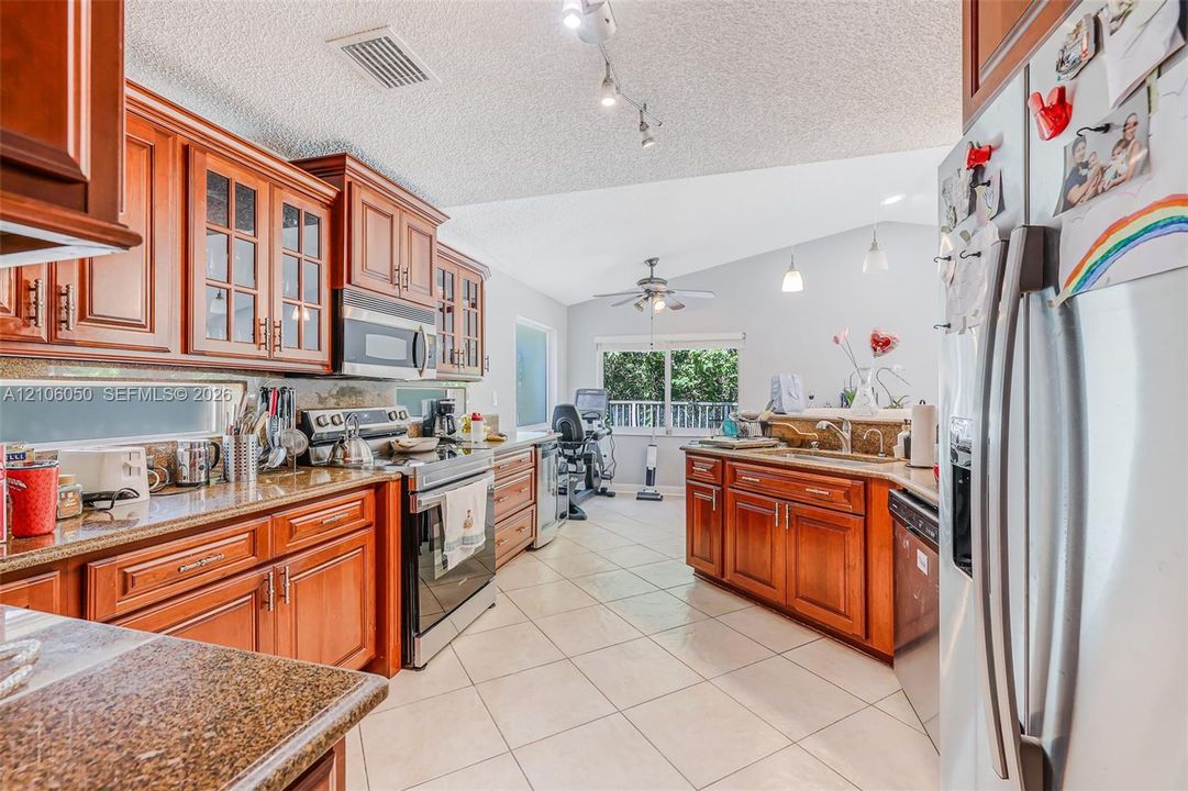 Kitchen featuring wood cabinetry, stone countertops, stainless steel appliances, ceramic tile flooring, and vaulted ceilings