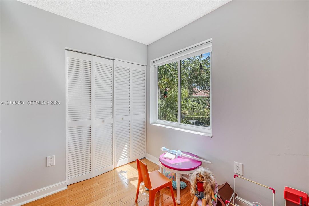 Bedroom featuring wood-finish flooring, a double-panel louvered closet, and a large horizontal window providing exterior greenery
