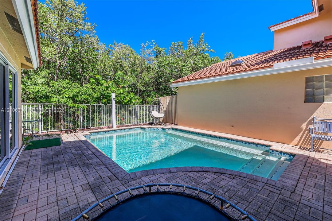 In-ground pool with built-in stairs, enclosed by metal perimeter fencing, featuring paver hardscaping and a clay tile roof