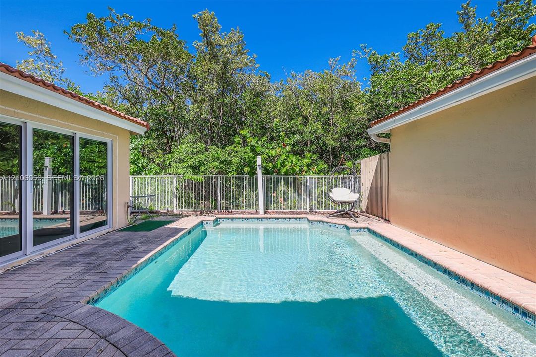 Private outdoor area featuring an in-ground swimming pool, stone-paver decking, sliding glass doors, and a metal perimeter fence