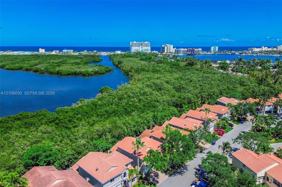Aerial perspective of a coastal residential community featuring tile roofs, lush natural vegetation, expansive waterways, and a clear horizon line