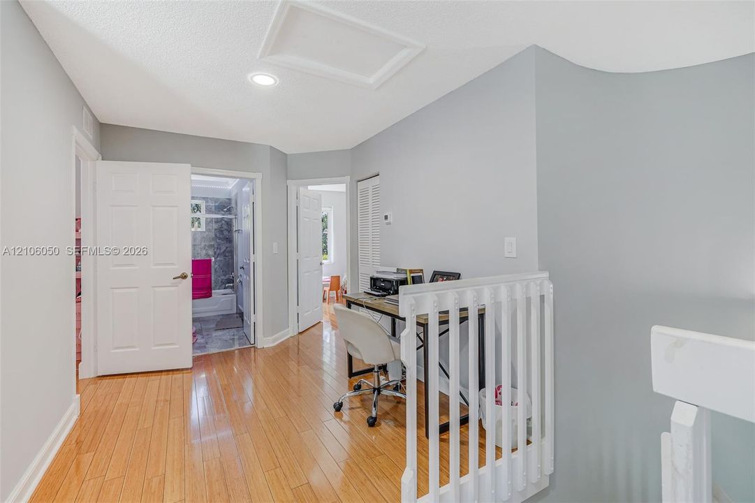 Interior hallway featuring wood-finish flooring, white paneled doors, recessed lighting, and a white vertical balustrade