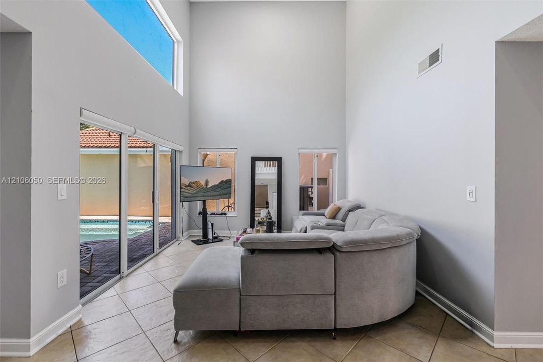 Double-height ceilings, ceramic tile flooring, expansive sliding glass doors, transom window, and dual vertical windows