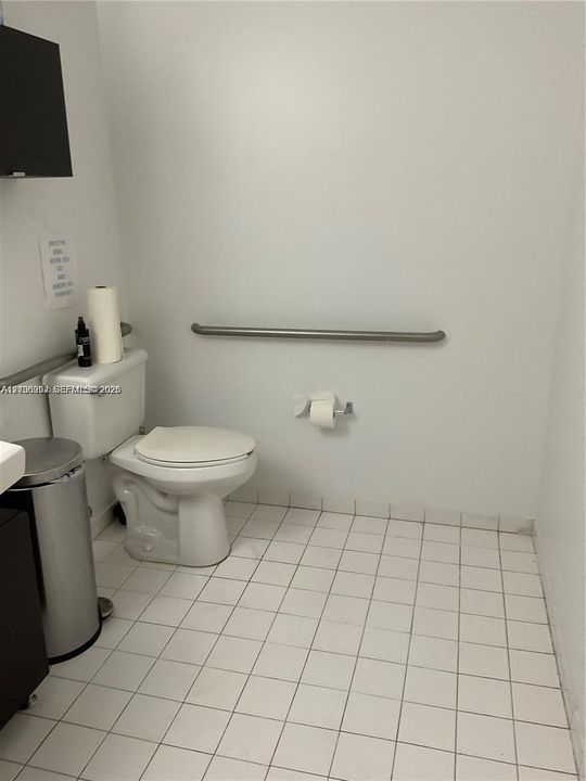 Restroom featuring white ceramic floor tiling, a porcelain toilet, and a mounted stainless steel grab bar
