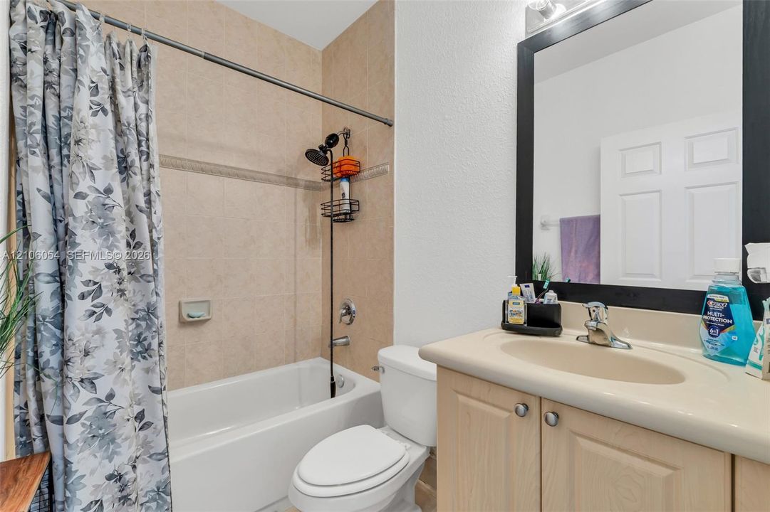 Bathroom featuring a vanity with an integrated countertop sink, neutral-toned tile shower surround, and a wall-mounted mirror with a dark frame