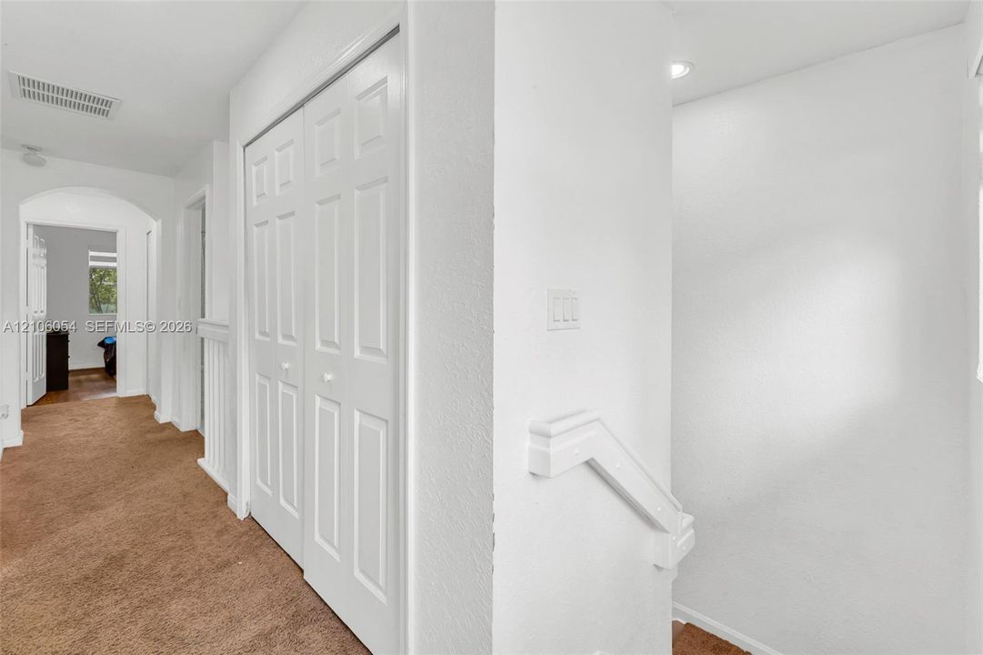 Hallway featuring carpeted flooring, a recessed ceiling light, white bifold closet doors, and a staircase with a white handrail