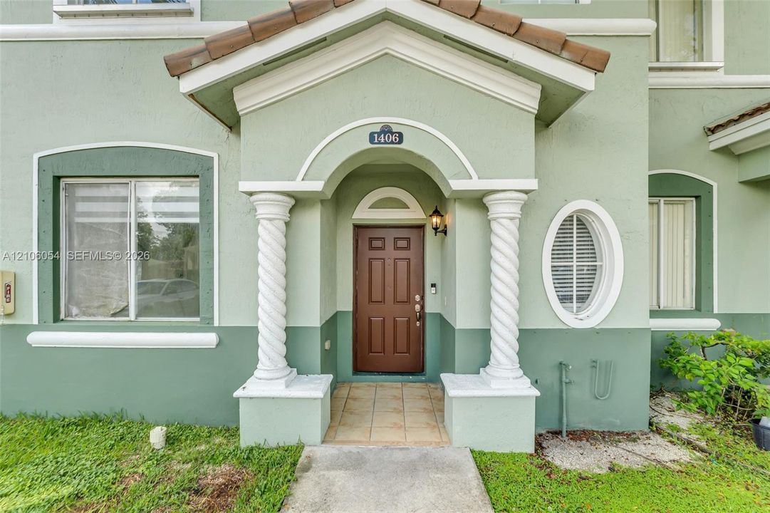 Exterior entrance featuring a covered porch with spiral columns, a tiled floor, an arched doorway, and an oval window