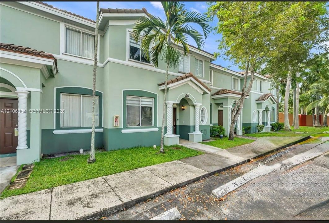 Two-story multi-family exterior featuring a stucco façade, covered entryway with decorative spiral columns, and tiled roof