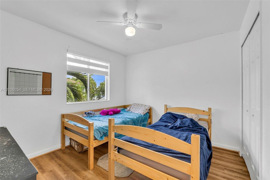 Neutral wall finish, wood-finish flooring, ceiling fan with integrated light fixture, horizontal window with white frame, and multi-panel sliding closet doors