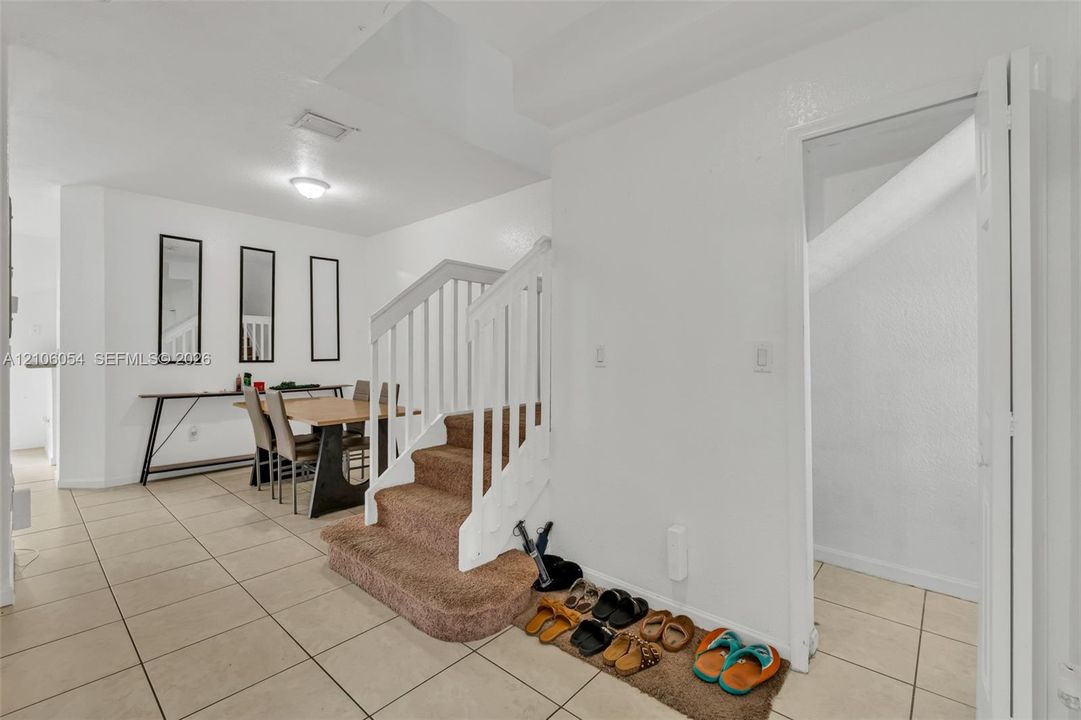 Staircase featuring a white balustrade, neutral carpeting, and tile flooring throughout the area