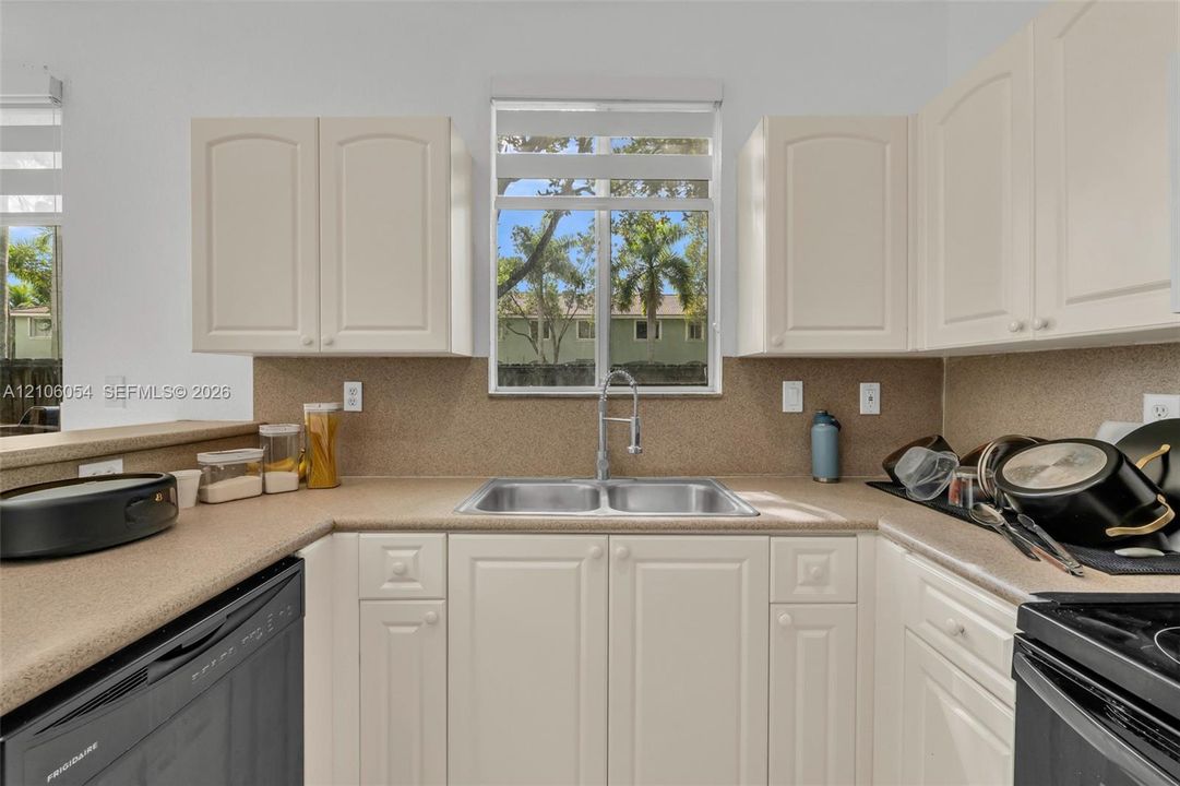 Kitchen featuring off-white cabinetry, solid-surface countertops, full-height backsplash, stainless steel dual-basin undermount sink, and a high-arc pull-down faucet