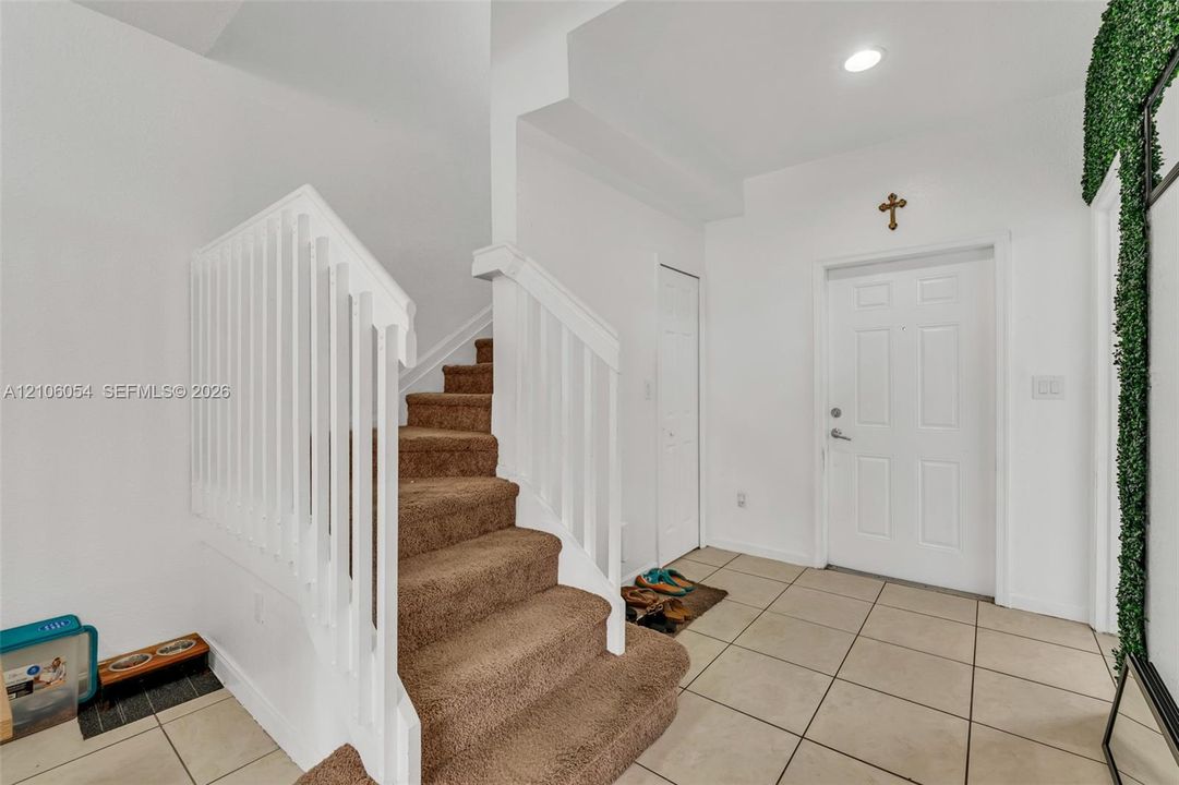 Entryway featuring ceramic tile flooring, a staircase with carpeted treads, and a white picket-style balustrade