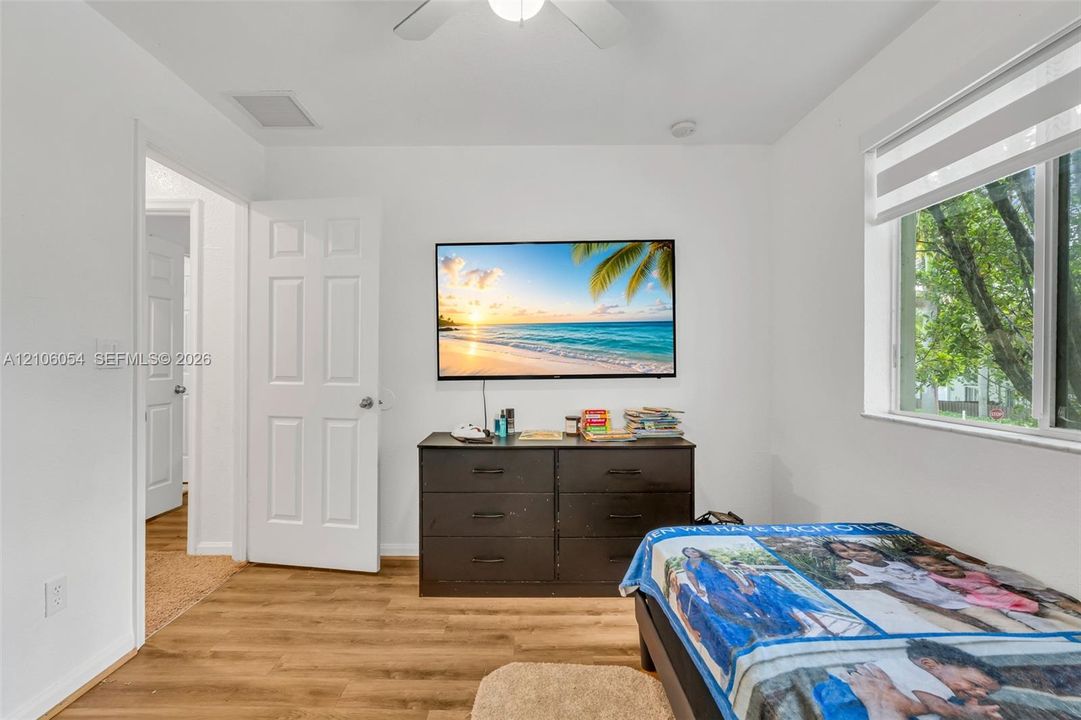 Room featuring wood-finish flooring, a ceiling fan, and a window with a fitted roller shade