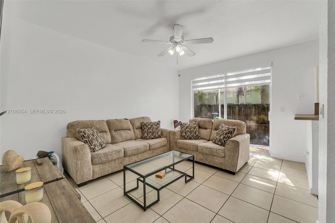 Neutral tile flooring, ceiling fan with integrated lighting, and large sliding glass door with horizontal blinds